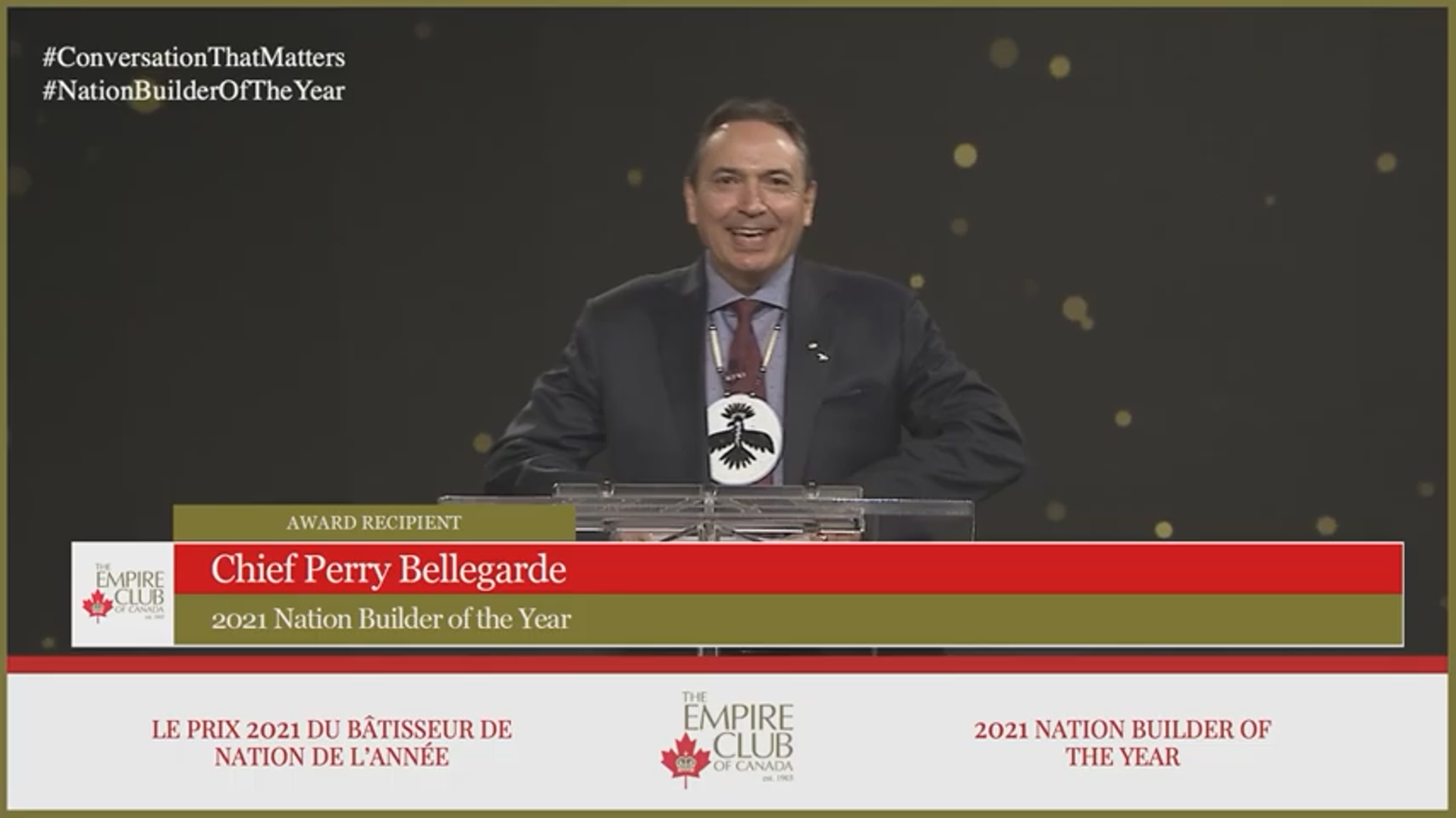 A man, Perry Bellegarde, smiling in front of a podium