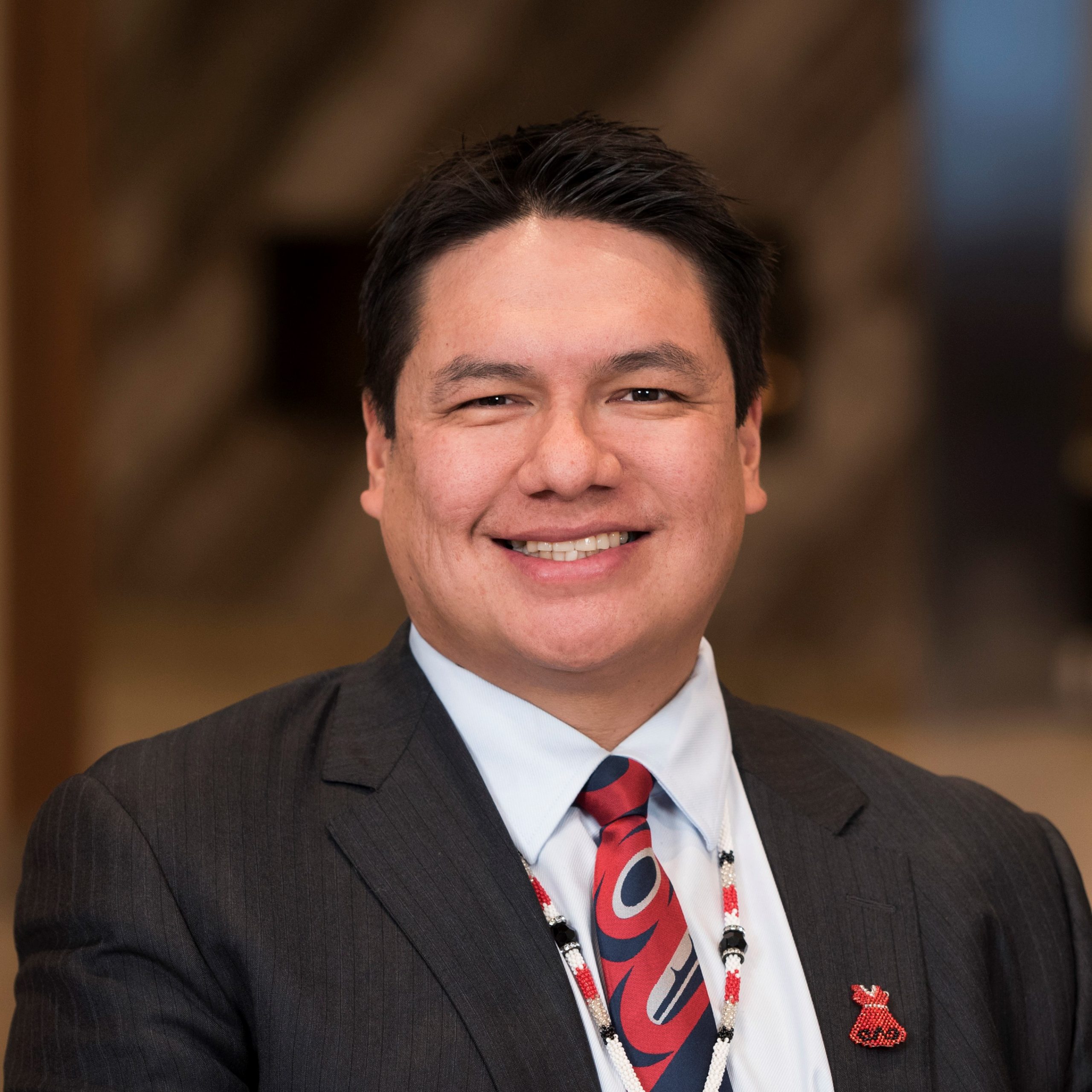 alt= A headshot of a man, Grand Chief Derek Fox, in a white collared shirt, black jacket, and red tie