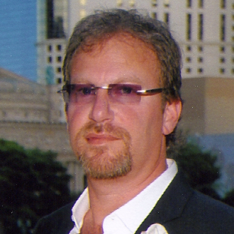 alt= Headshot of a man, Russ Fromm, against a skyscape, wearing purple glasses