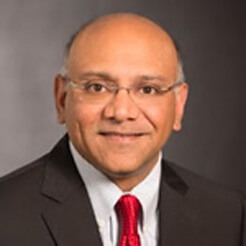 alt= Headshot of a man, Suresh Venkatesan, in a red tie, white shirt, and black jacket