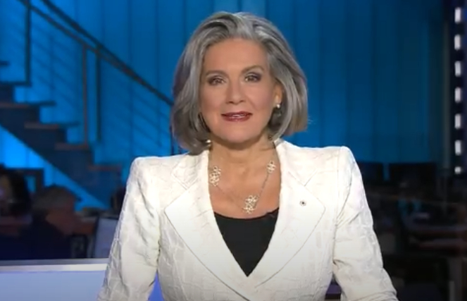 alt= Professional woman wearing a white suit jacket in a news studio.