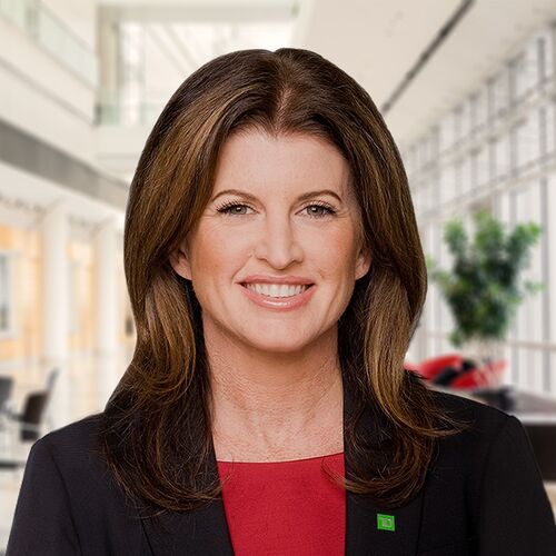 alt= Smiling woman, Former Minister of Health of Canada, wearing a black suit and red undershirt with a green TD Bank pin.