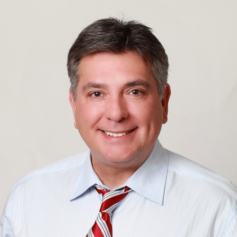 A man, Charles Sousa, in white shirt and red tie, smiling