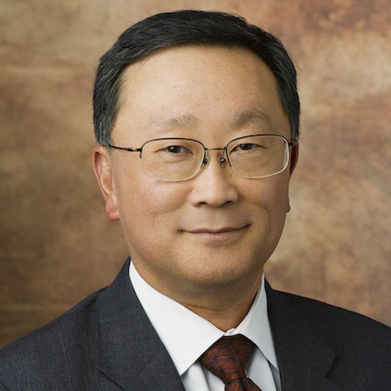 a man, John Chen, smiling, wearing black jacket , white shirt and a red tie
