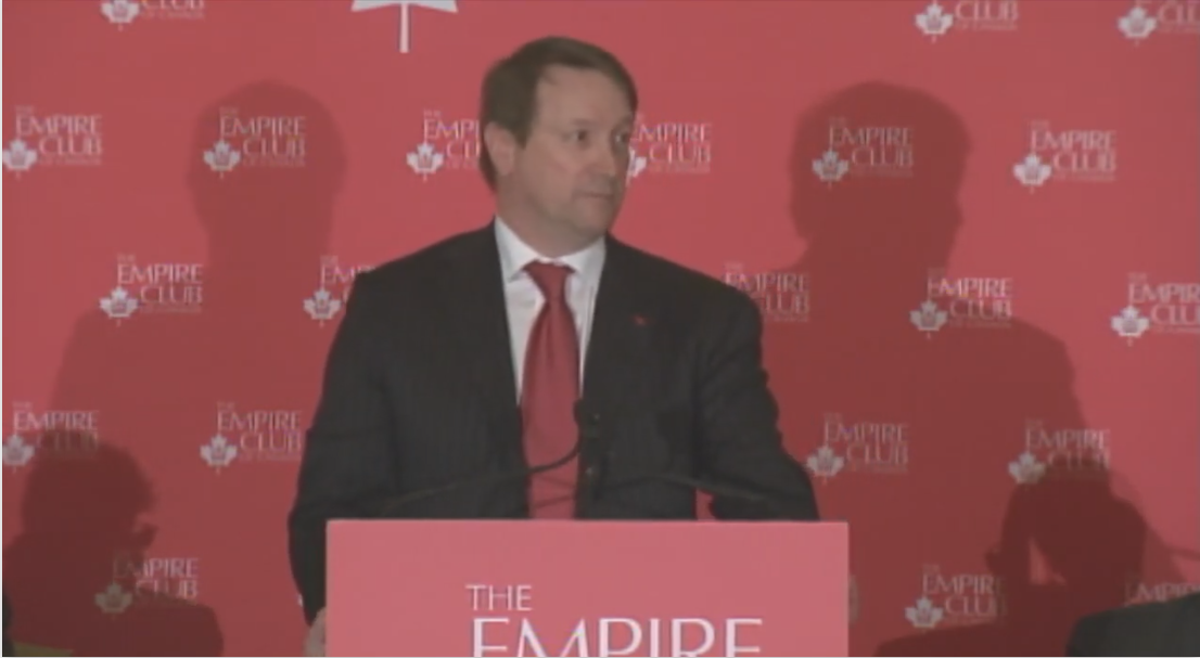 man in a dark suit and red tie delivers keynote speech from Empire Club of Canada podium
