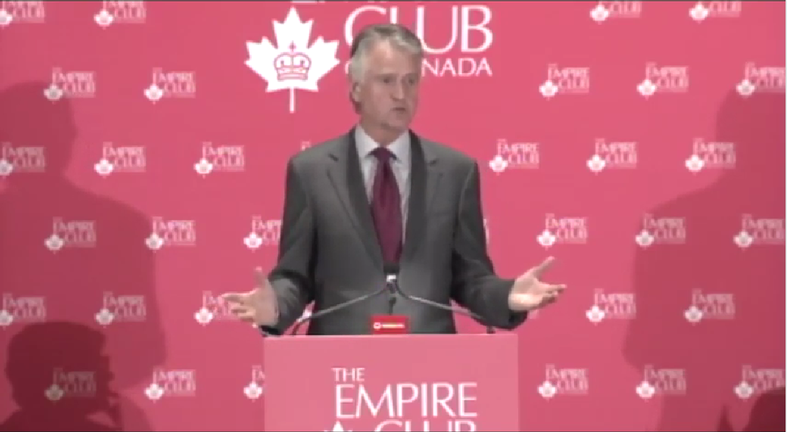 a man in a grey suit delivering a keynote suit from the Empire Club of Canada podium