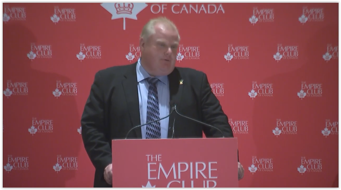 a man in a dark suit delivering a keynote speech from the Empire Club of Canada's podium