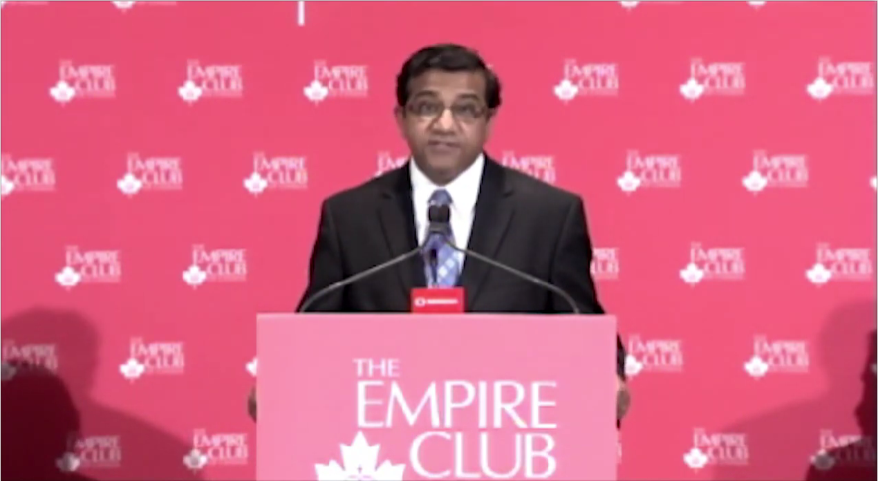 a man in a dark suit delivering a keynote speech from the Empire Club of Canada podium