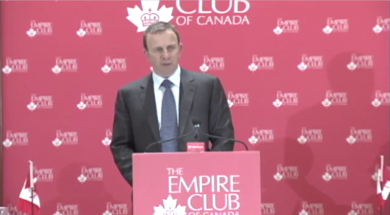 man in a grey suit and blue tie delivering a keynote speech at the Empire Club of Canada's podium