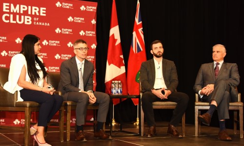 A woman and three men are engaging in a panel discussion at Empire Club of Canada